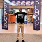 Author standing with his arms wide in front of a sign that says Freedom School