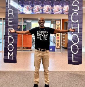 Author standing with his arms wide in front of a sign that says Freedom School